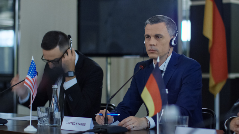 Internationale Konferenzteilnehmer mit Headsets folgen der Simultanverdolmetschung – US-amerikanische und deutsche Delegation